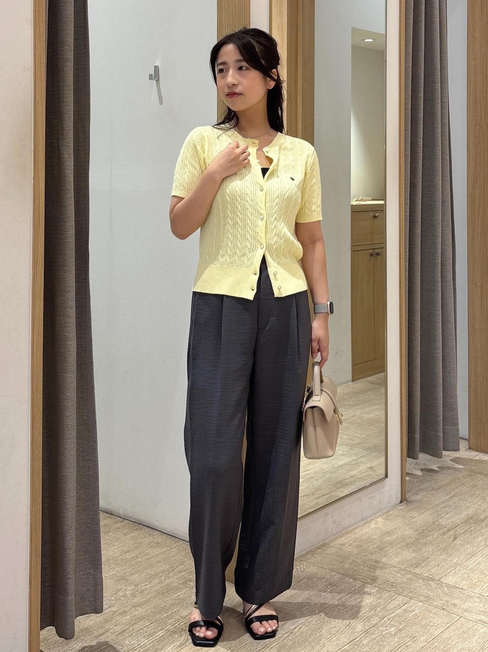 ベージュ系のショルダーバッグ、ブラック系のサンダル、グレー系のスラックスを着用したレディースの夏コーディネートの1枚目の写真