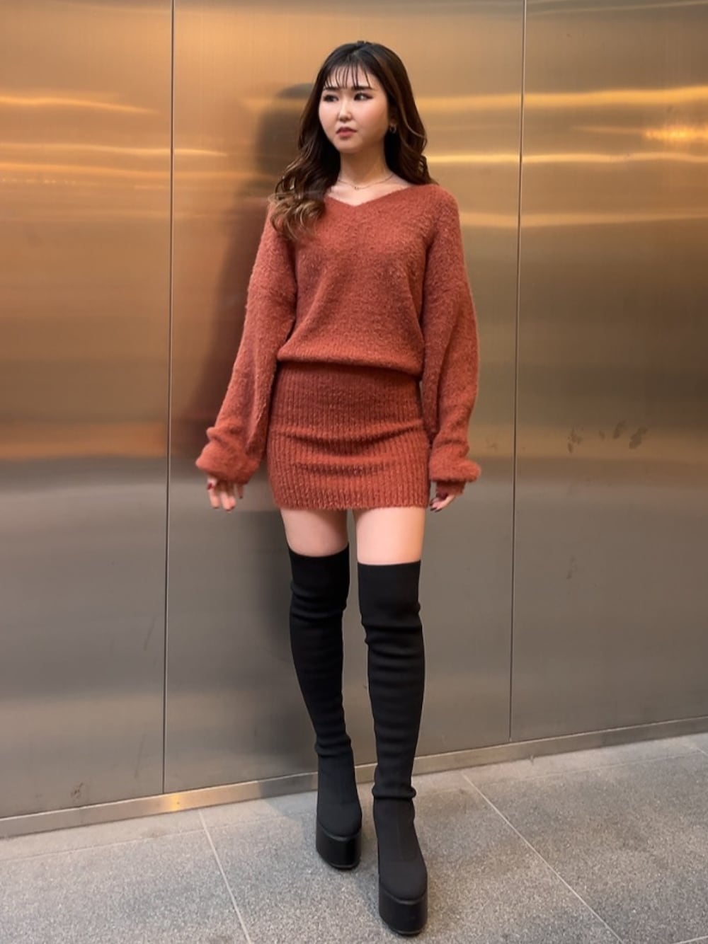 オレンジ系のワンピース、ブラック系のブーツを着用したレディースの冬コーディネートの1枚目の写真