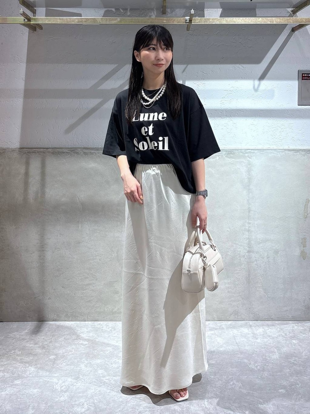 ホワイト系のスカート、ホワイト系のサンダル、ブラック系のTシャツ/カットソーを着用したレディースの夏コーディネートの1枚目の写真