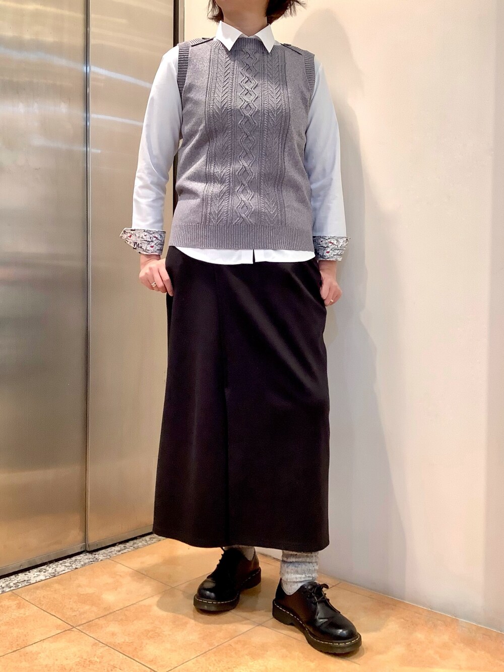 ホワイト系のビジネスシャツ、グレー系のベストを着用したレディースの春コーディネートの1枚目の写真