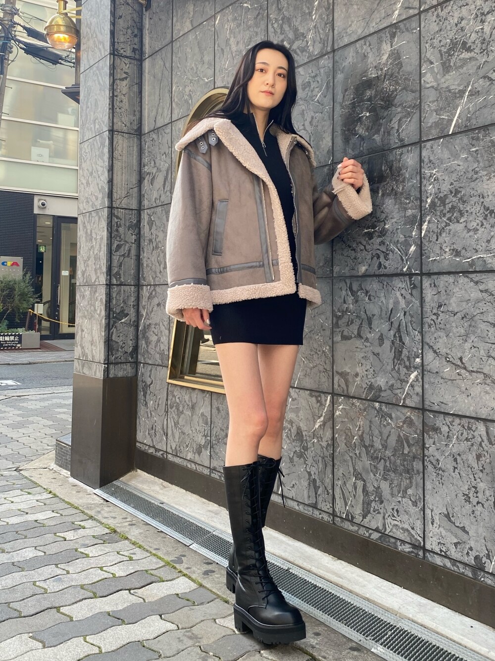 グレー系のブルゾン、ブラック系のワンピース、ブラック系のブーツを着用したレディースの冬コーディネートの1枚目の写真