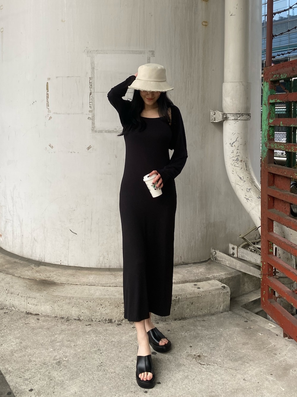 ブラック系のワンピース、ブラック系のサンダル、ホワイト系のハットを着用したレディースの春コーディネートの1枚目の写真