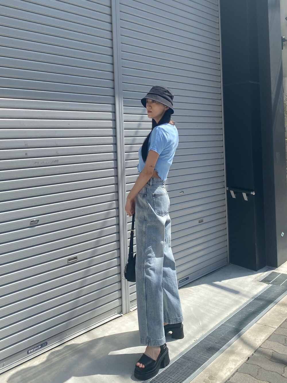 ブルー系のデニムパンツ、ブラック系のサンダル、ブラック系のハンドバッグを着用したレディースの夏コーディネートの1枚目の写真