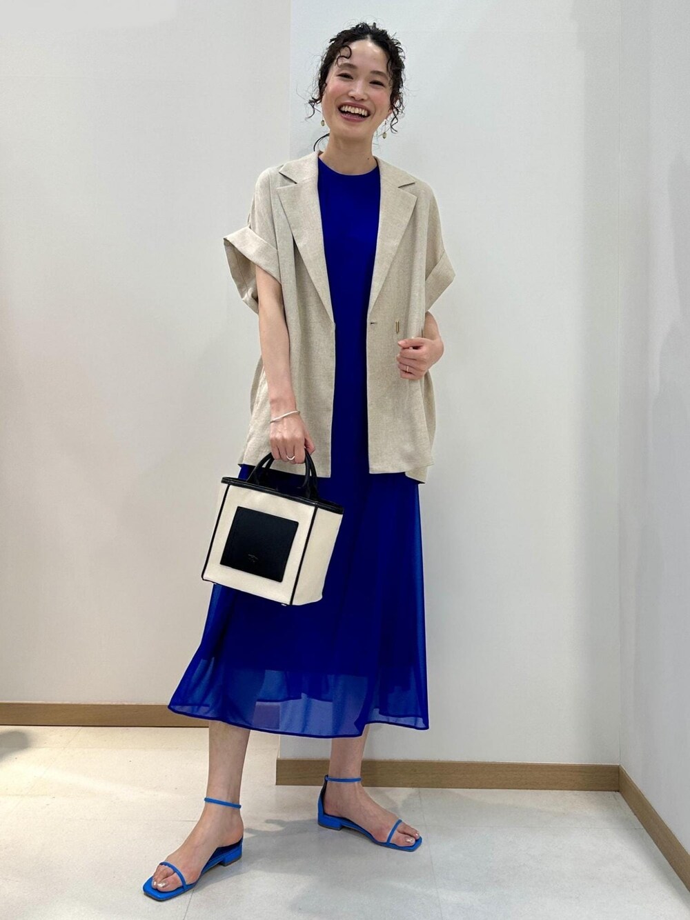 ブラック系のトートバッグ、ブルー系のサンダル、ブルー系のワンピースを着用したレディースの春コーディネートの1枚目の写真