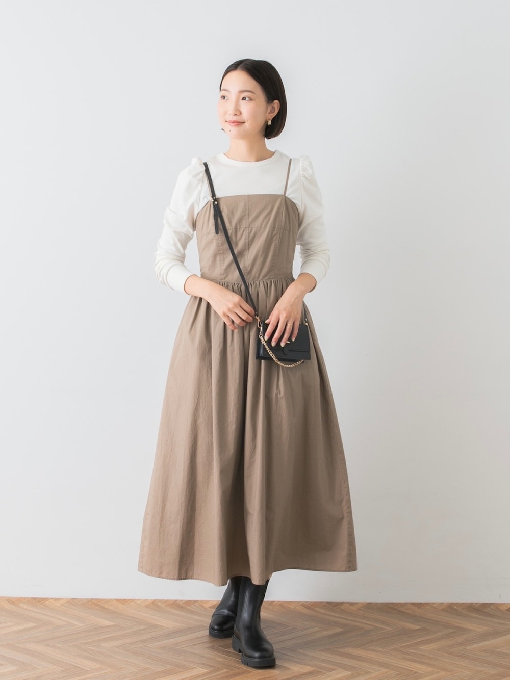 ベージュ系のワンピース、ホワイト系のTシャツ/カットソー、ブラック系のブーツを着用したレディースの秋コーディネートの1枚目の写真