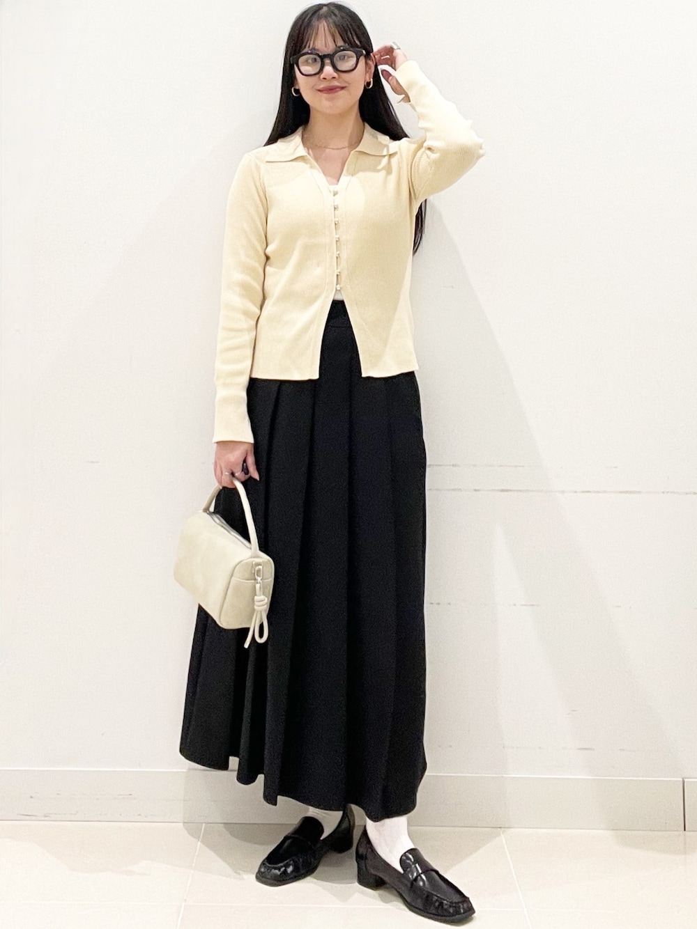 ブラック系のローファー、ブラック系のスカート、ベージュ系のハンドバッグを着用したレディースの春コーディネートの1枚目の写真