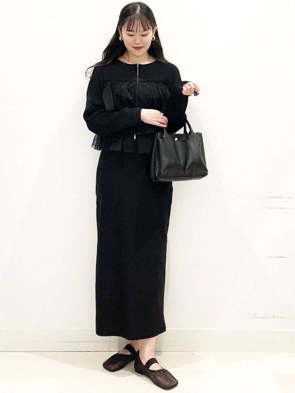 ブラック系のニット/セーター、ブラック系のスカート、ブラック系のトートバッグを着用したレディースの春コーディネートの1枚目の写真