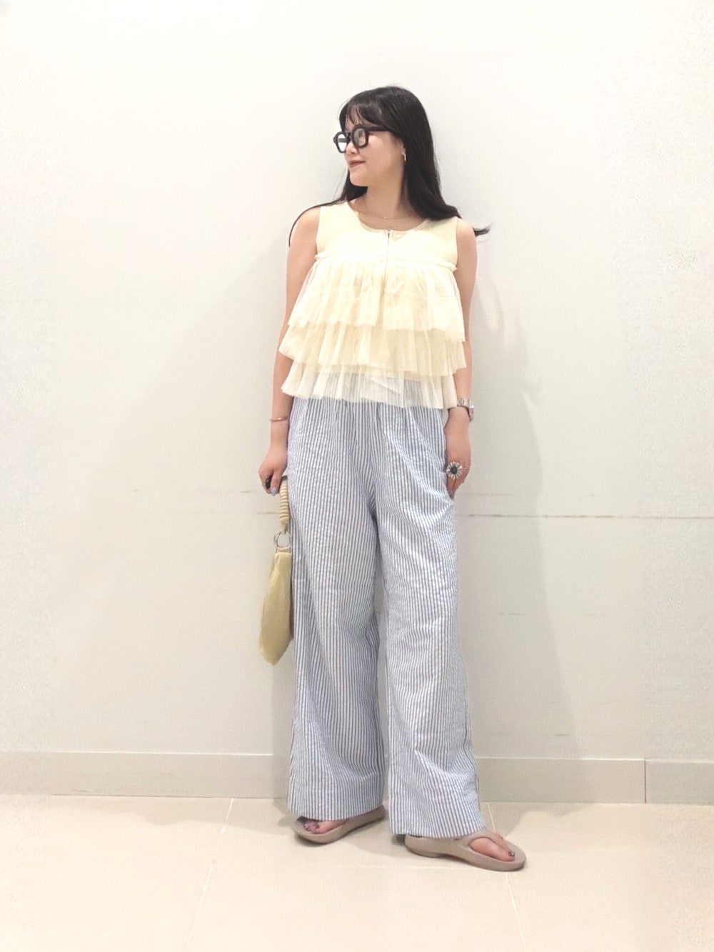 イエロー系のニット/セーター、ベージュ系のハンドバッグ、ベージュ系のサンダルを着用したレディースの夏コーディネートの1枚目の写真