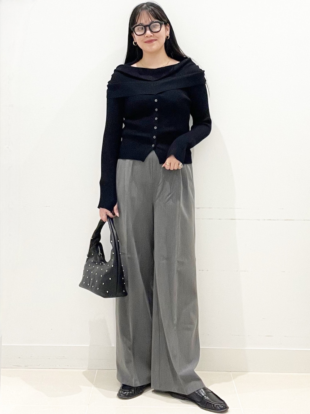 グレー系のスラックス、ブラック系のハンドバッグ、ブラック系のニット/セーターを着用したレディースの春コーディネートの1枚目の写真