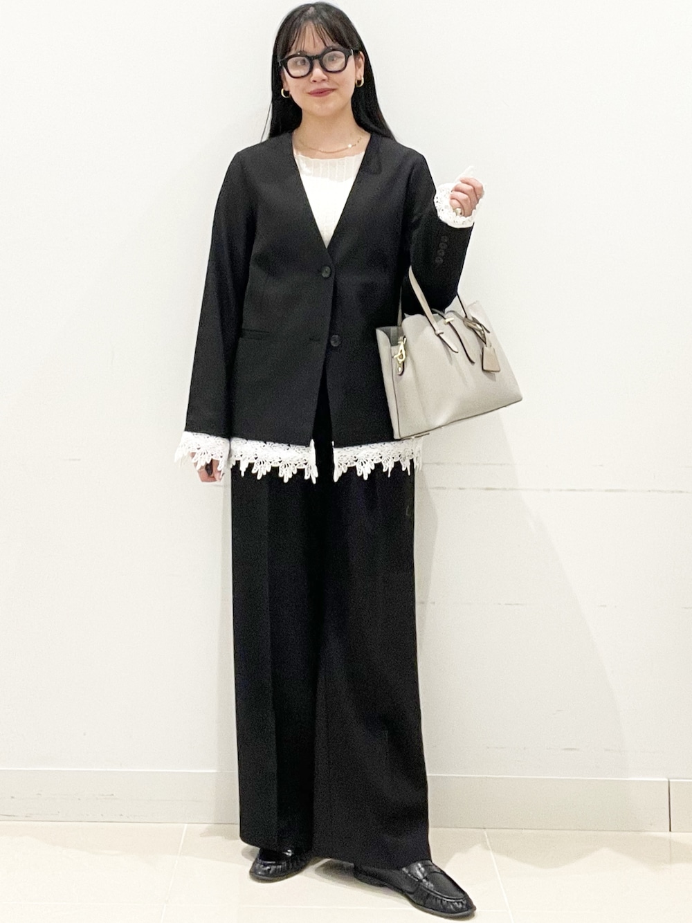 ブラック系のスラックス、グレー系のトートバッグ、ブラック系のノーカラージャケットを着用したレディースの春コーディネートの1枚目の写真