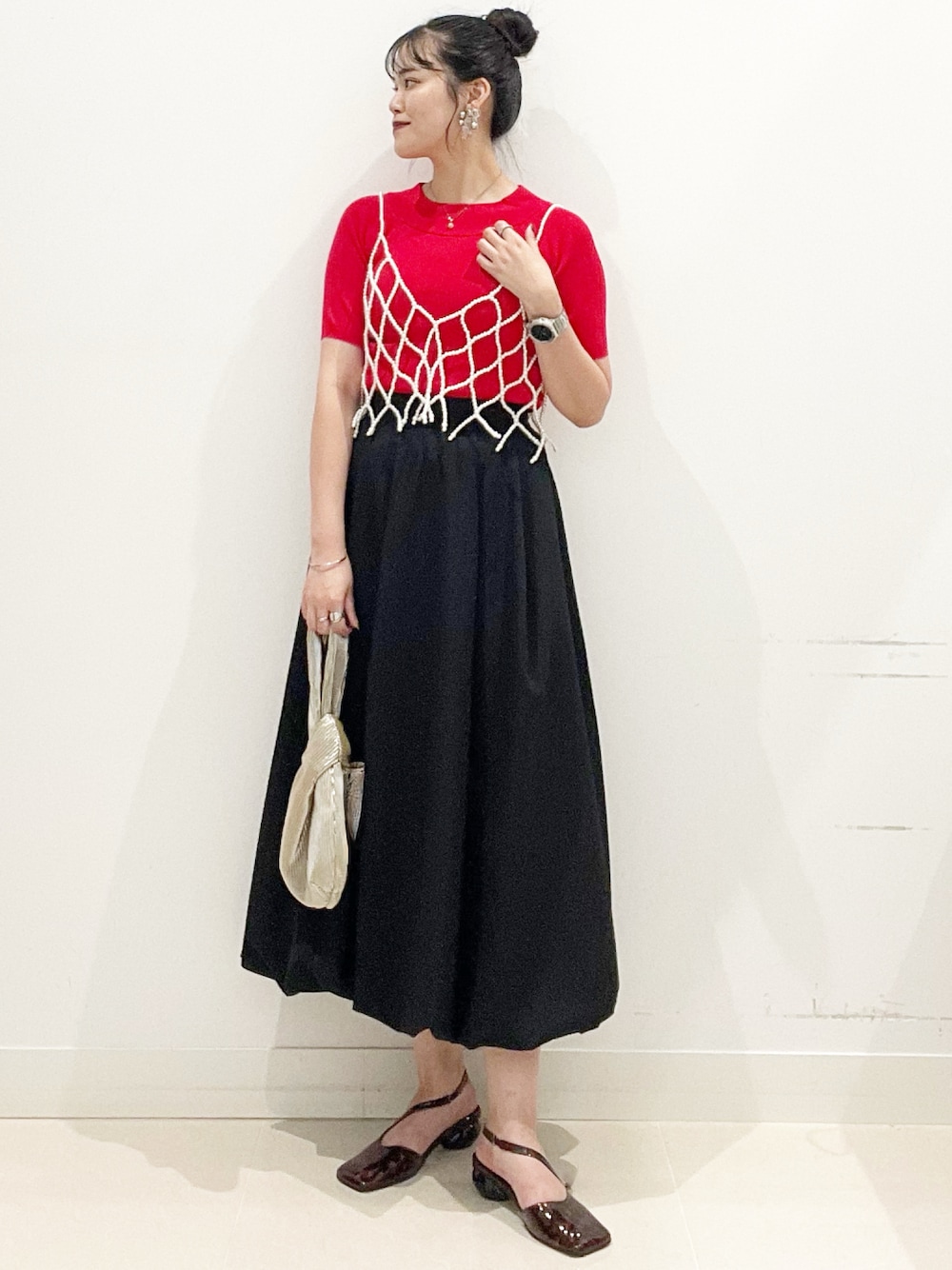 ブラック系のスカート、ゴールド系のハンドバッグ、レッド系のニット/セーターを着用したレディースの夏コーディネートの1枚目の写真