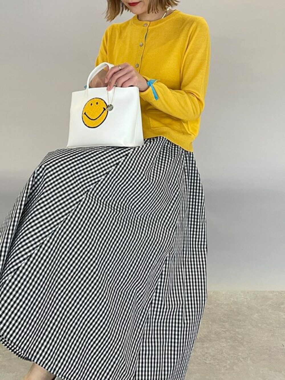 イエロー系のカーディガン/ボレロ、ブラック系のスカートを着用したレディースの春コーディネートの1枚目の写真