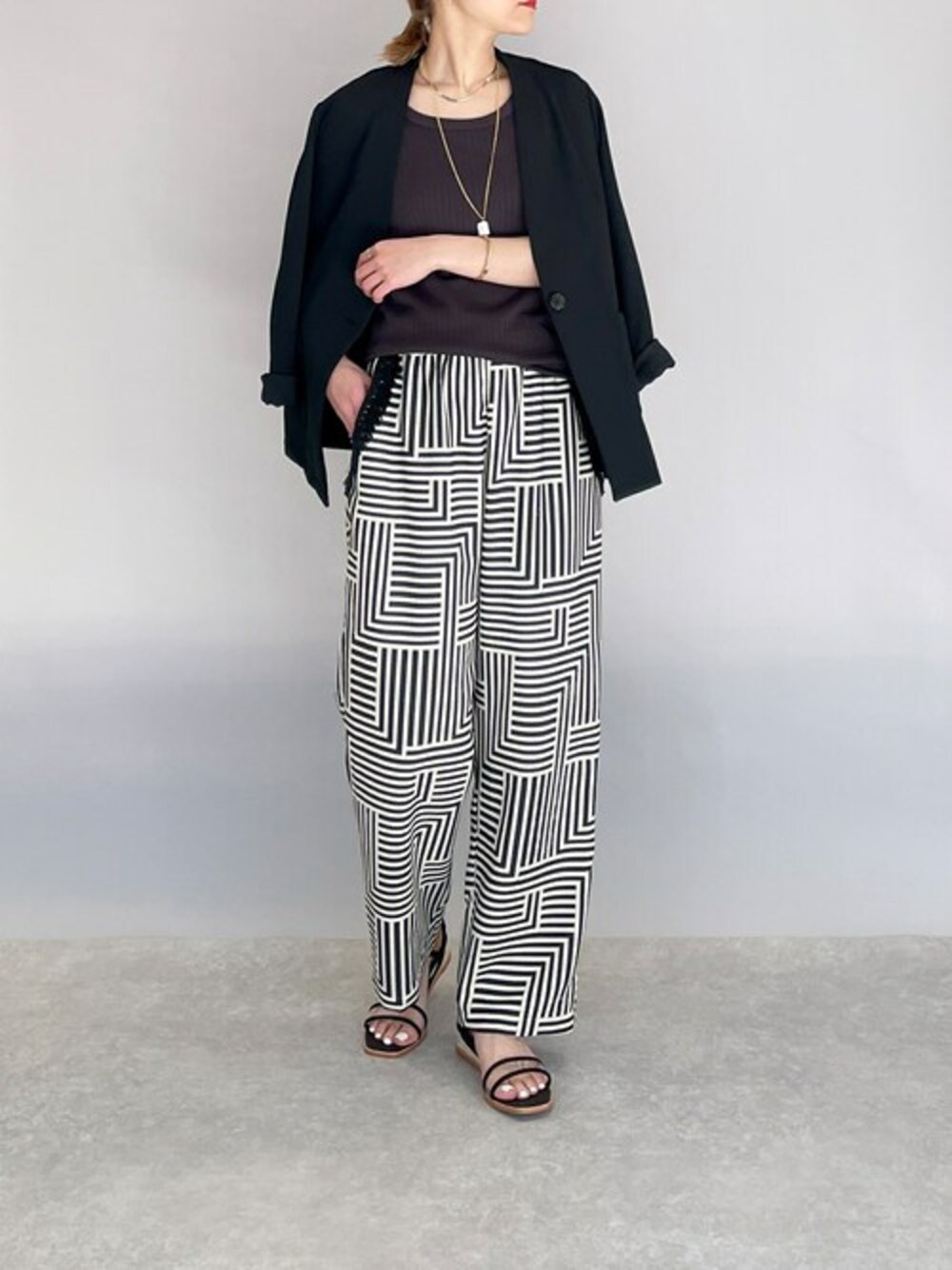 ブラック系のテーラードジャケット、グレー系のタンクトップ、ブラック系のサンダルを着用したレディースの春コーディネートの1枚目の写真