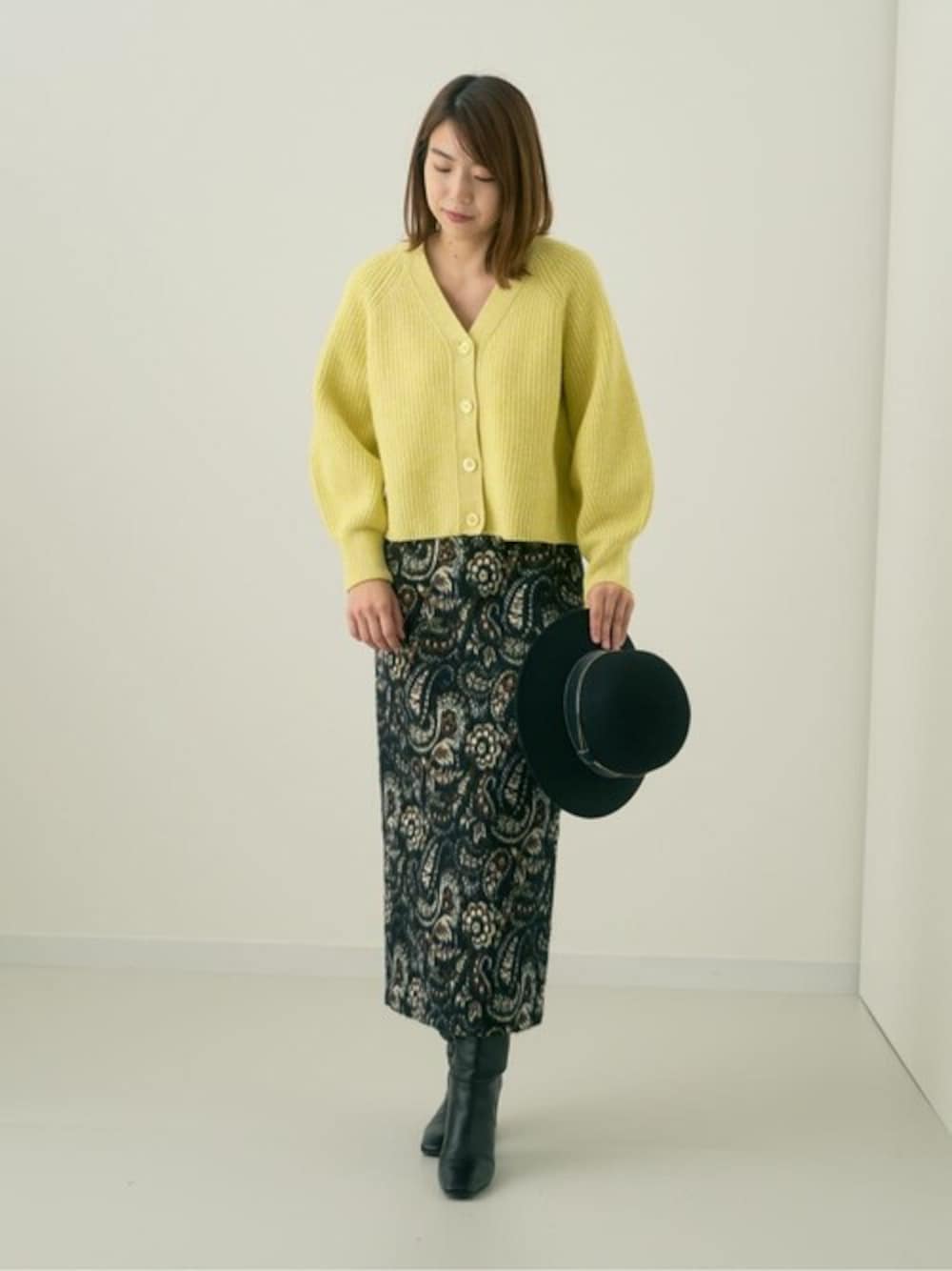 イエロー系のカーディガン/ボレロ、ブラック系のスカートを着用したレディースの秋コーディネートの1枚目の写真