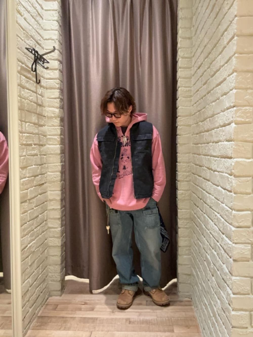 ブルー系のデニムパンツ、ブラック系のベスト、ピンク系のパーカーを着用したメンズの秋コーディネートの1枚目の写真