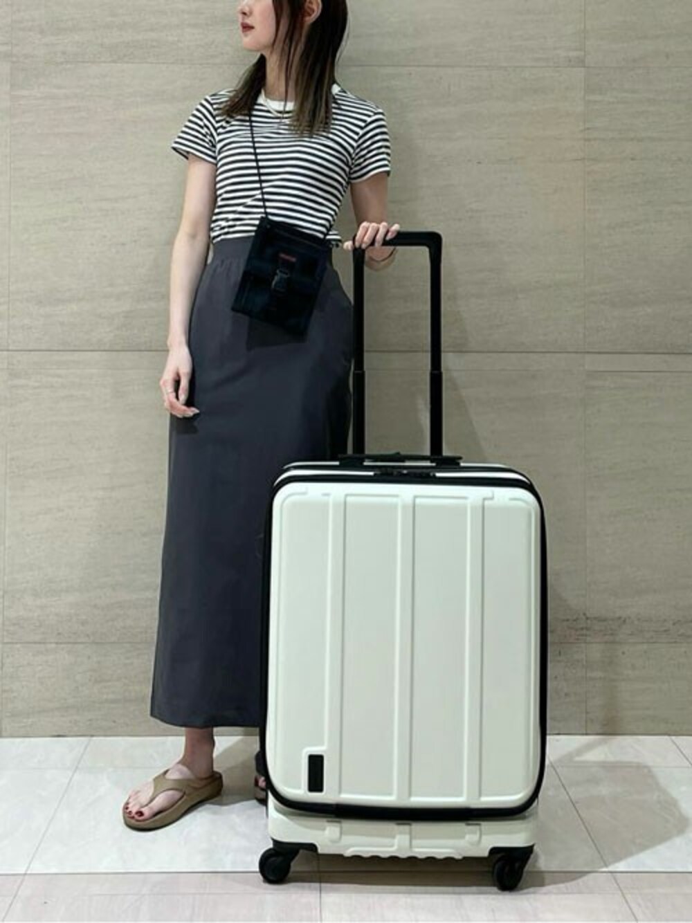 シルバー系のスーツケース/キャリーバッグ、ブラック系のショルダーバッグを着用したレディースの夏コーディネートの1枚目の写真