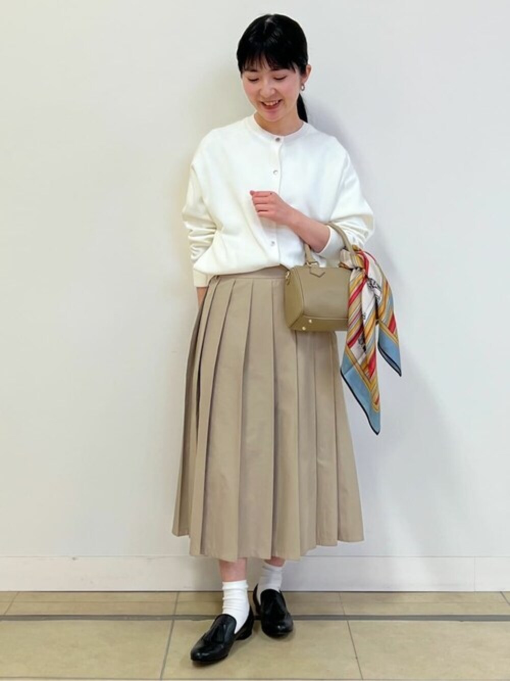 ホワイト系のカーディガン/ボレロ、ベージュ系のスカート、ベージュ系のボストンバッグを着用したレディースの春コーディネートの1枚目の写真