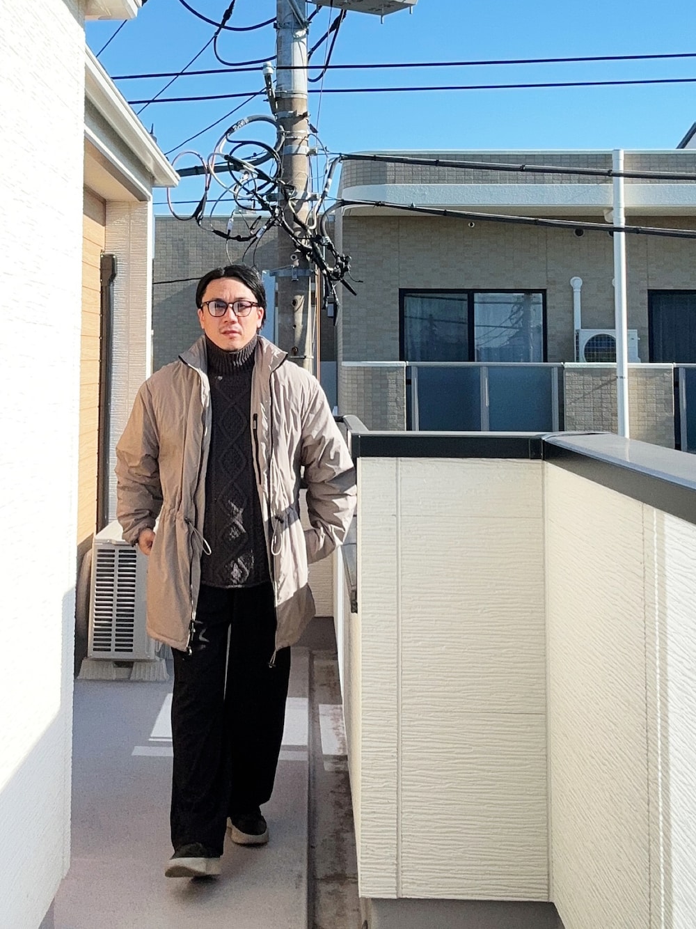 ブラック系のニット/セーター、ベージュ系のその他アウター、ブラック系のスニーカーを着用したメンズの冬コーディネートの1枚目の写真