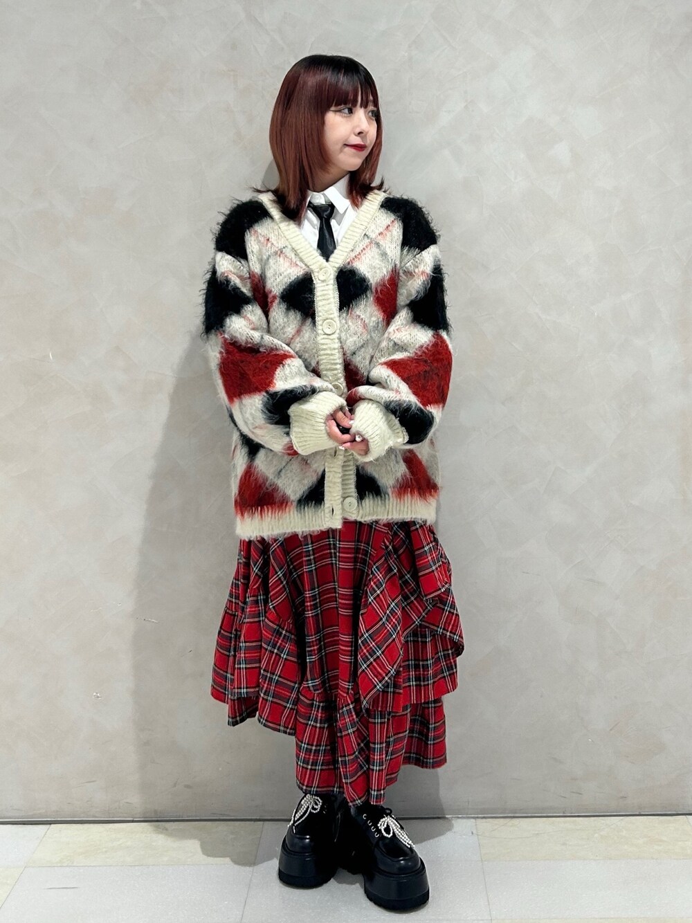 レッド系のスカート、ブラック系のドレスシューズ、ホワイト系のカーディガン/ボレロを着用したレディースの秋コーディネートの1枚目の写真