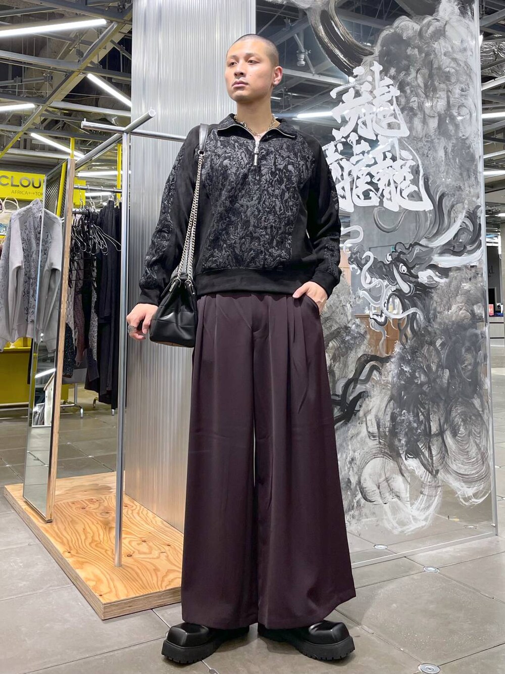 レッド系のスラックス、ブラック系のドレスシューズ、ブラック系のショルダーバッグを着用したメンズの冬コーディネートの1枚目の写真