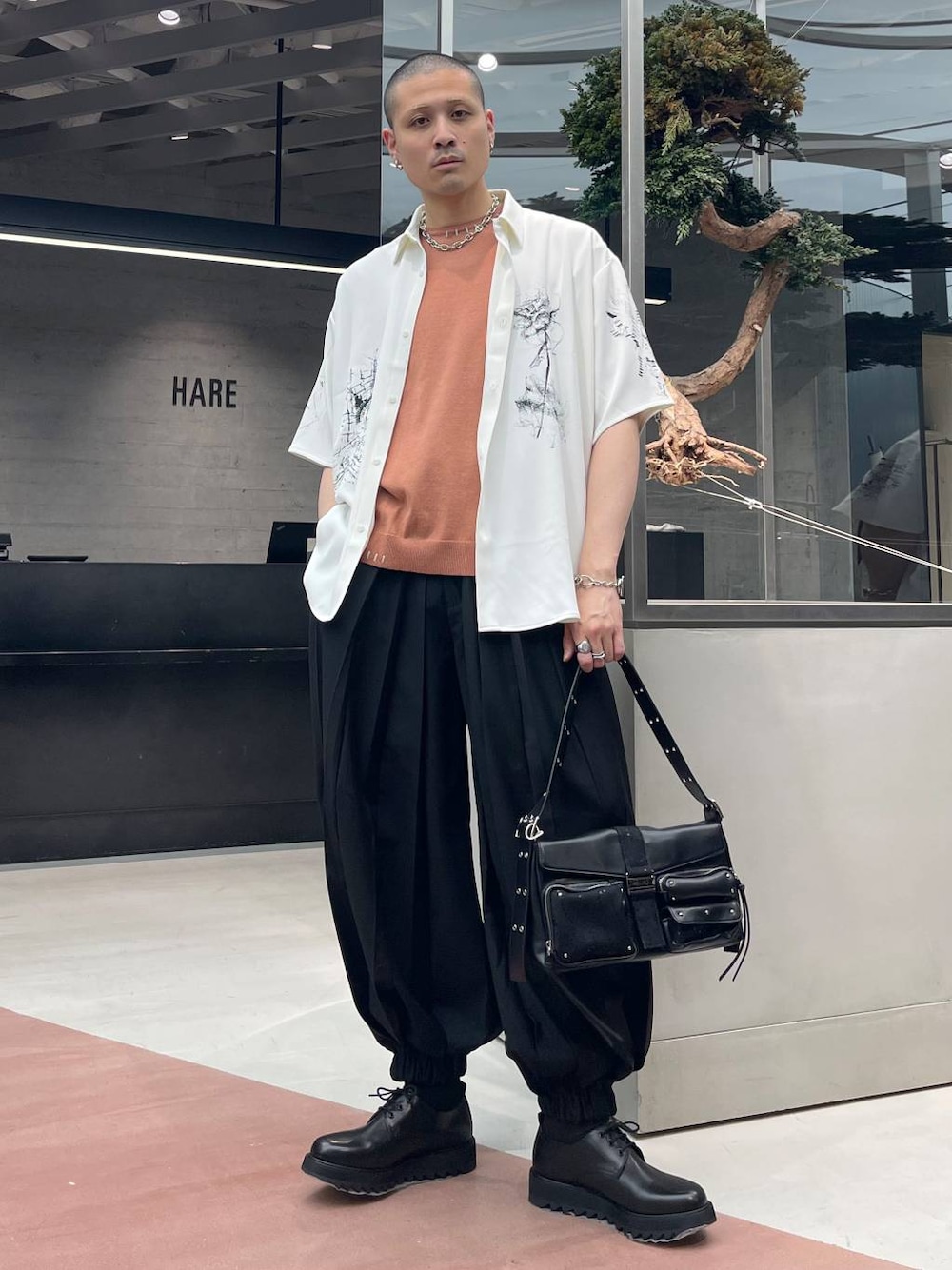 ブラック系のショルダーバッグ、ブラック系のその他パンツ、オレンジ系のニット/セーターを着用したメンズの春コーディネートの1枚目の写真
