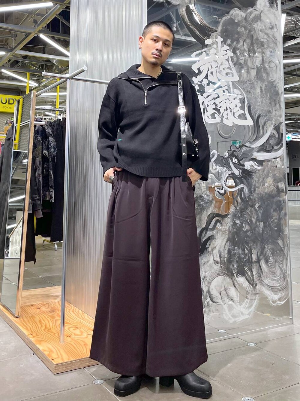 レッド系のスラックス、ブラック系のブーツ、ブラック系のニット/セーターを着用したメンズの秋コーディネートの1枚目の写真