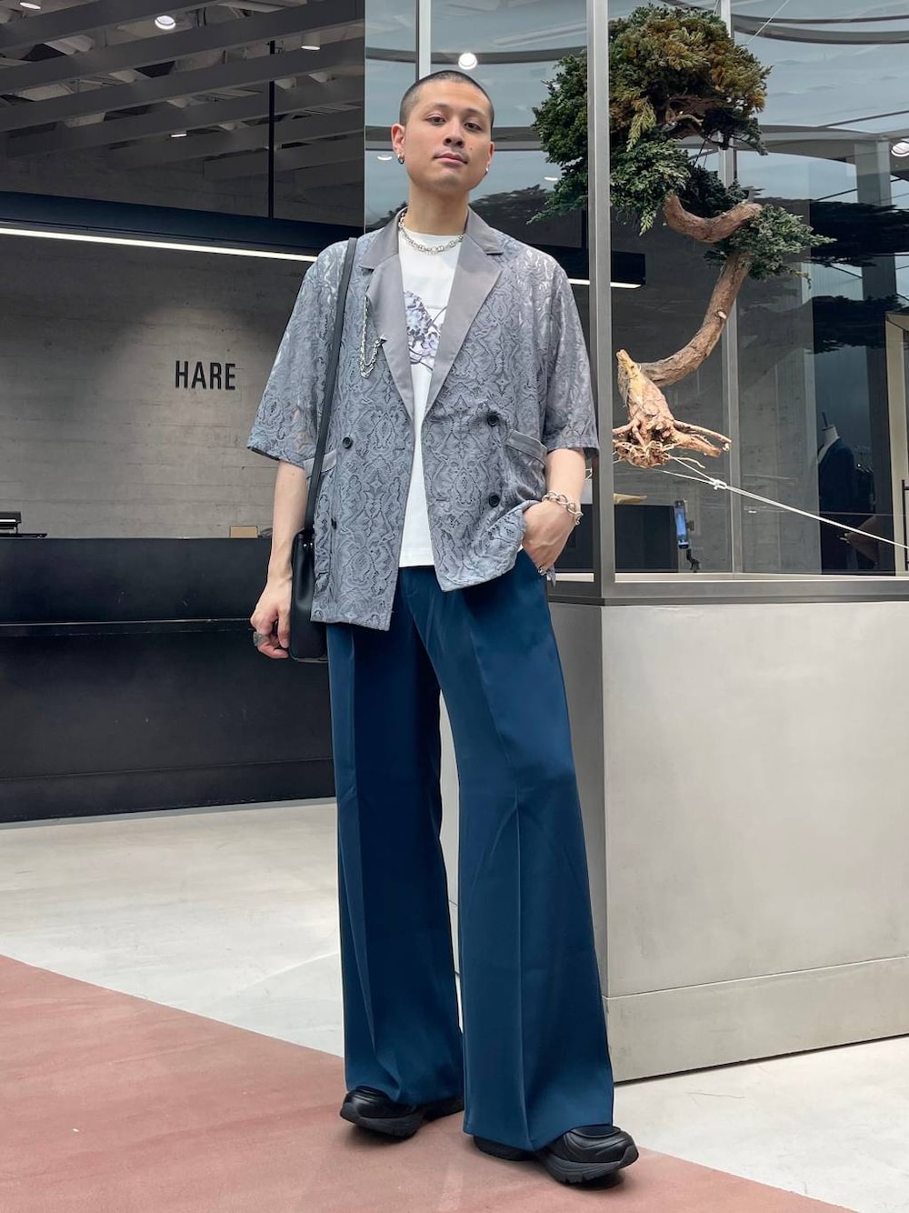 ブルー系のスラックス、ブラック系のショルダーバッグ、ホワイト系のTシャツ/カットソーを着用したメンズの夏コーディネートの1枚目の写真