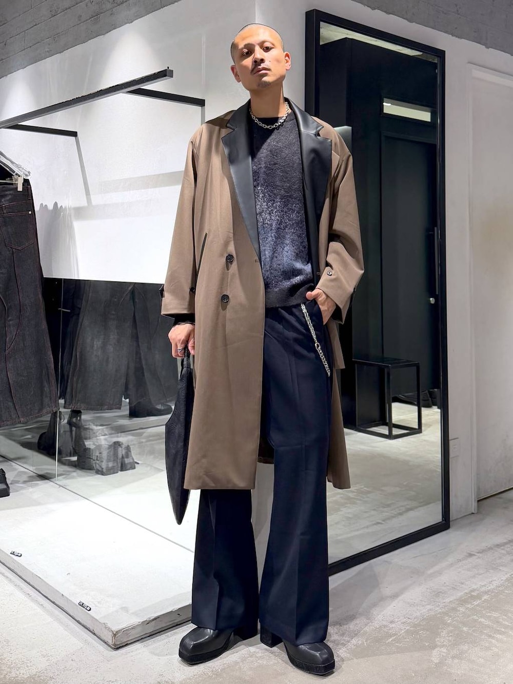 ブラック系のニット/セーター、ベージュ系のチェスターコート、ブラック系のトートバッグを着用したメンズの秋コーディネートの1枚目の写真