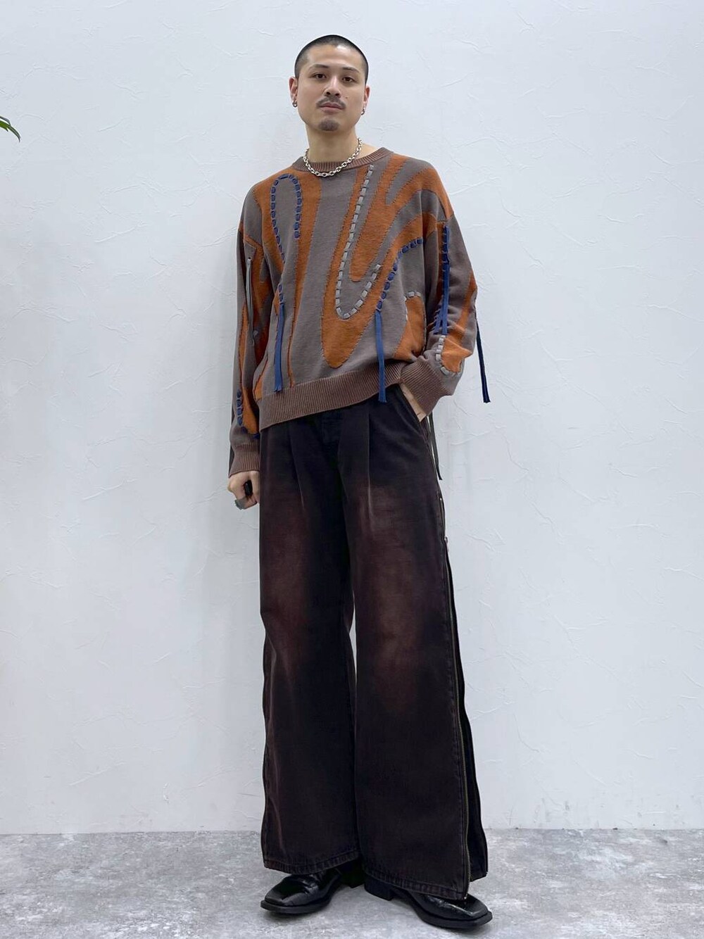 レッド系のデニムパンツ、ブラウン系のニット/セーター、ブラック系のブーツを着用したメンズの夏コーディネートの1枚目の写真