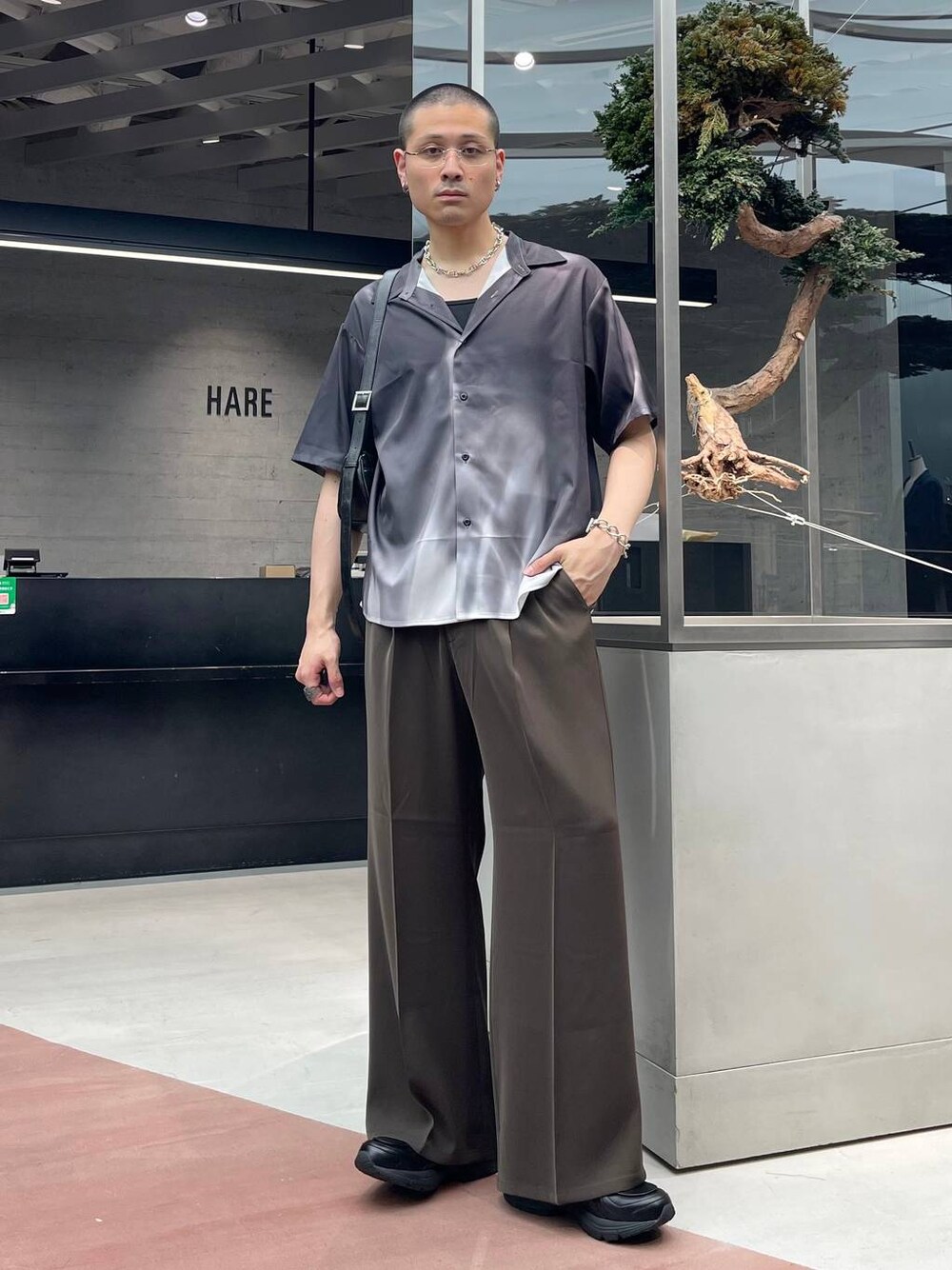 ブラウン系のスラックス、ブラック系のショルダーバッグ、ブラック系のシャツ/ブラウスを着用したメンズの夏コーディネートの1枚目の写真