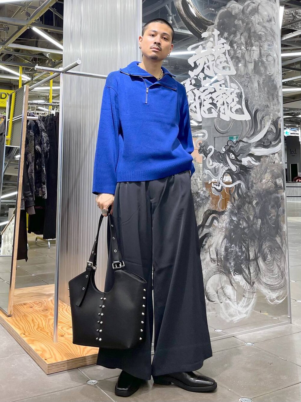 グレー系のスラックス、ブラック系のブーツ、ブルー系のニット/セーターを着用したメンズの秋コーディネートの1枚目の写真