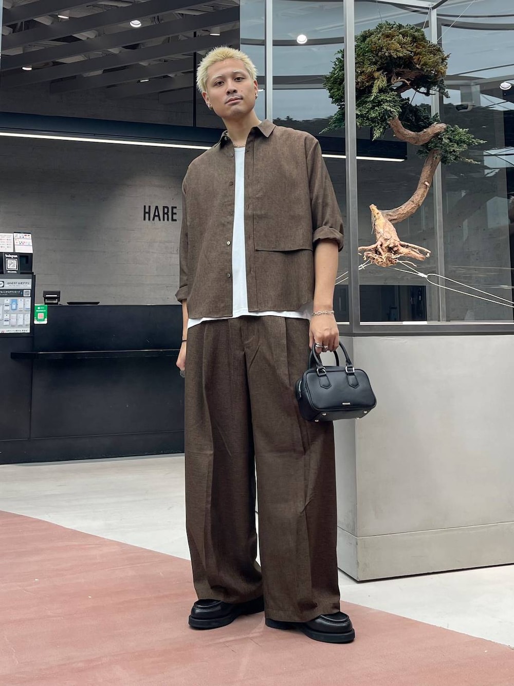 ブラウン系のスラックス、ブラック系のローファー、ブラック系のボストンバッグを着用したメンズの夏コーディネートの1枚目の写真