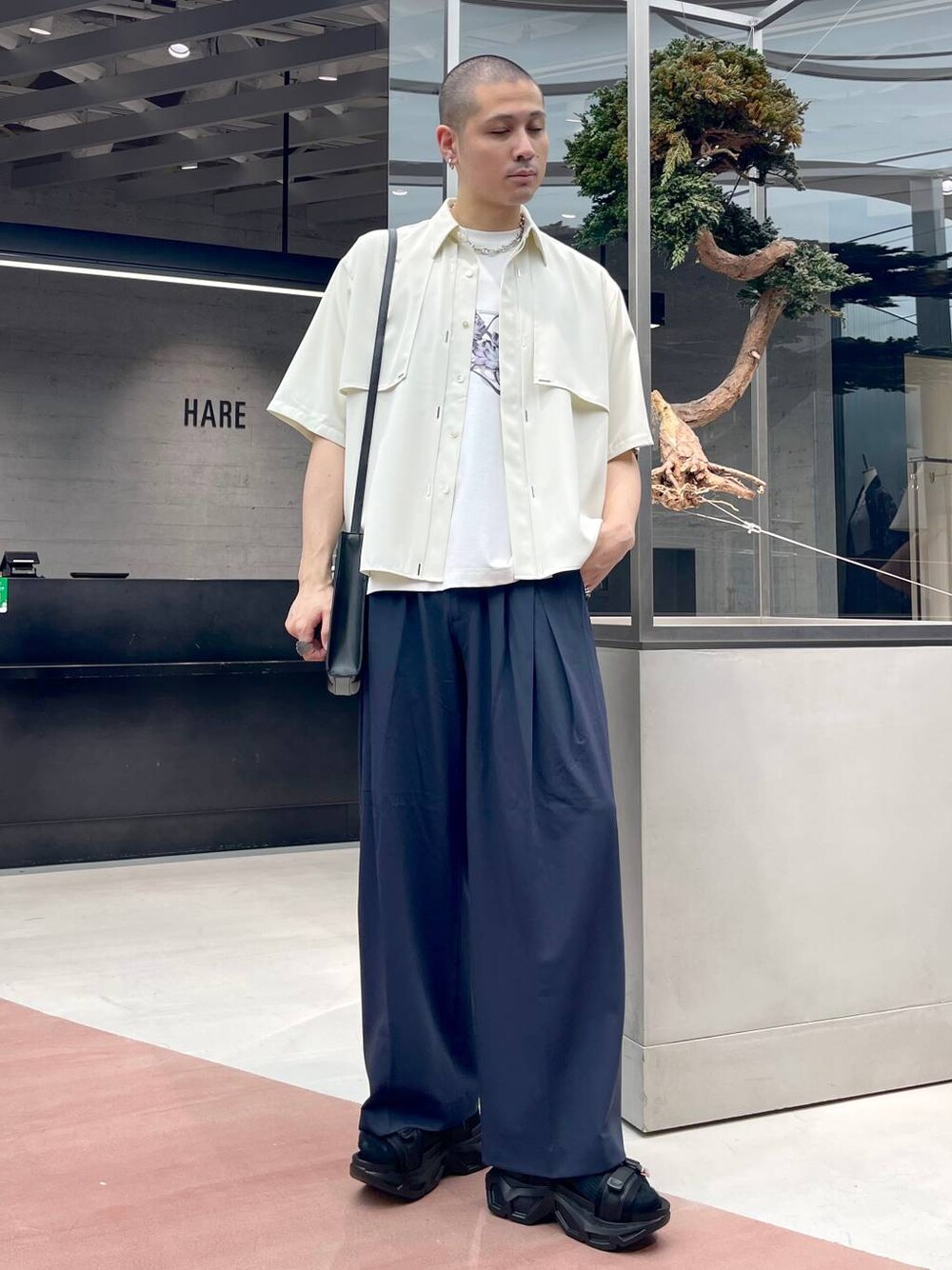 ブラック系のショルダーバッグ、ブラック系のサンダル、ブルー系のスラックスを着用したメンズの夏コーディネートの1枚目の写真