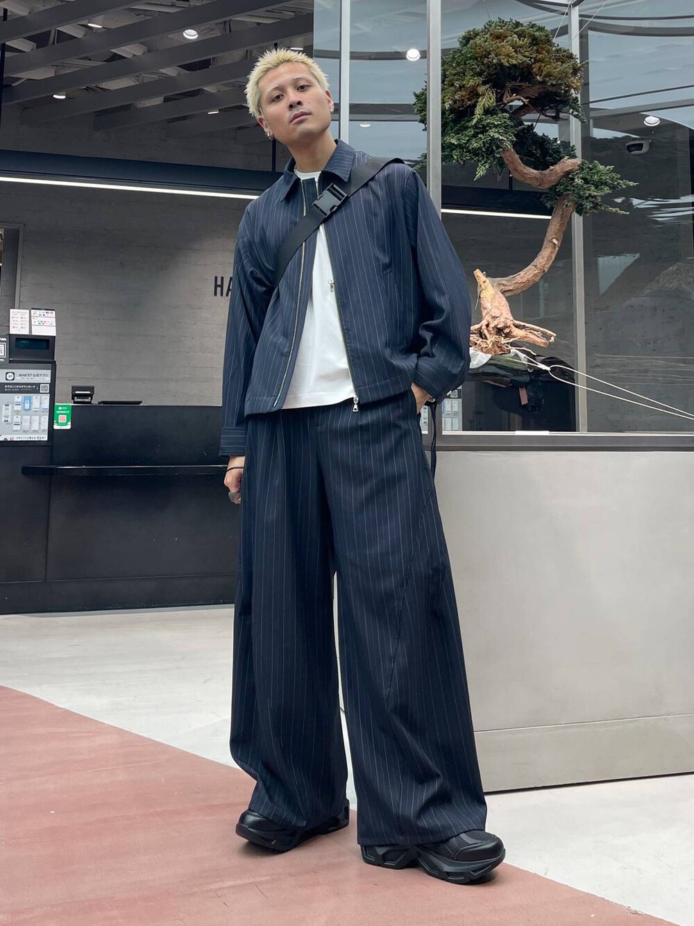 ブラック系のメッセンジャーバッグ、ブルー系のスラックス、ブルー系のブルゾンを着用したメンズの秋コーディネートの1枚目の写真