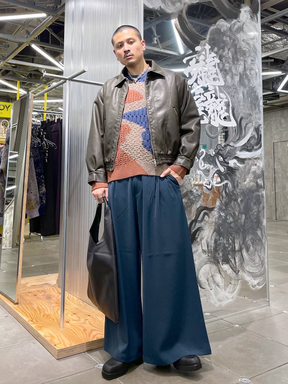 ブラック系のトートバッグ、ブルー系のスラックス、ブラック系のブーツを着用したメンズの冬コーディネートの1枚目の写真