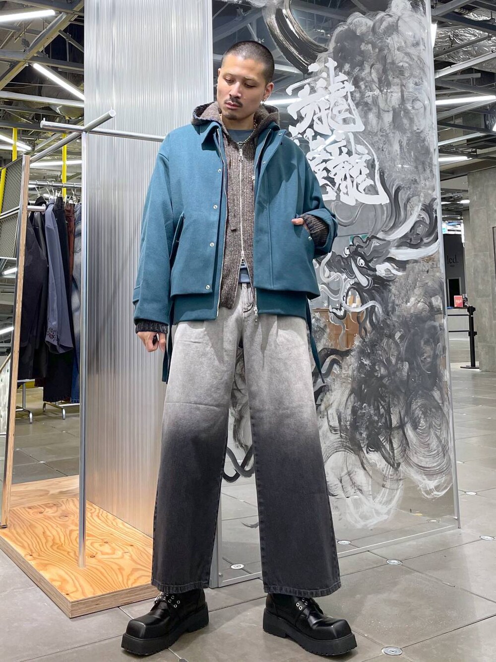 グリーン系のブルゾン、ブラック系のドレスシューズ、ブラウン系のニット/セーターを着用したメンズの秋コーディネートの1枚目の写真