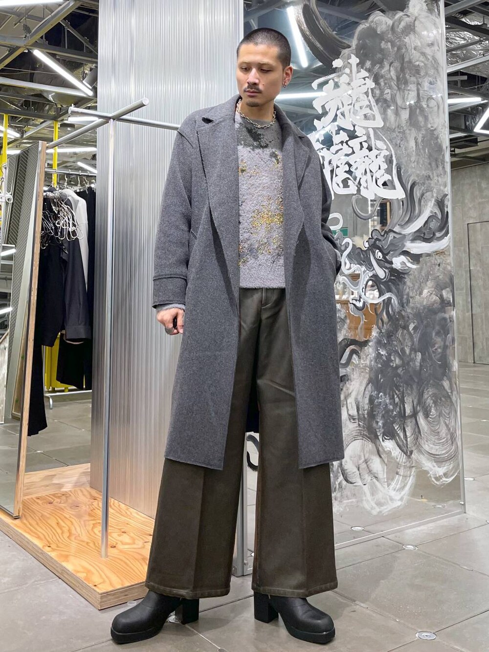 グレー系のトレンチコート、ブラウン系のその他パンツ、ブラック系のブーツを着用したメンズの冬コーディネートの1枚目の写真