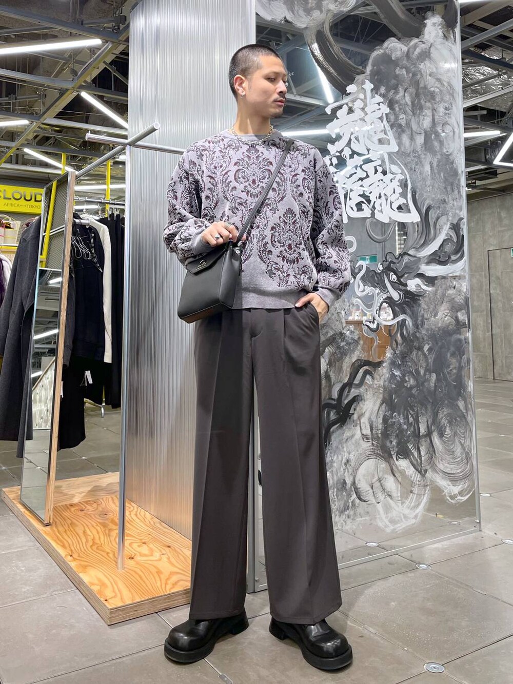 グレー系のニット/セーター、ブラック系のショルダーバッグ、ブラウン系のスラックスを着用したメンズの冬コーディネートの1枚目の写真