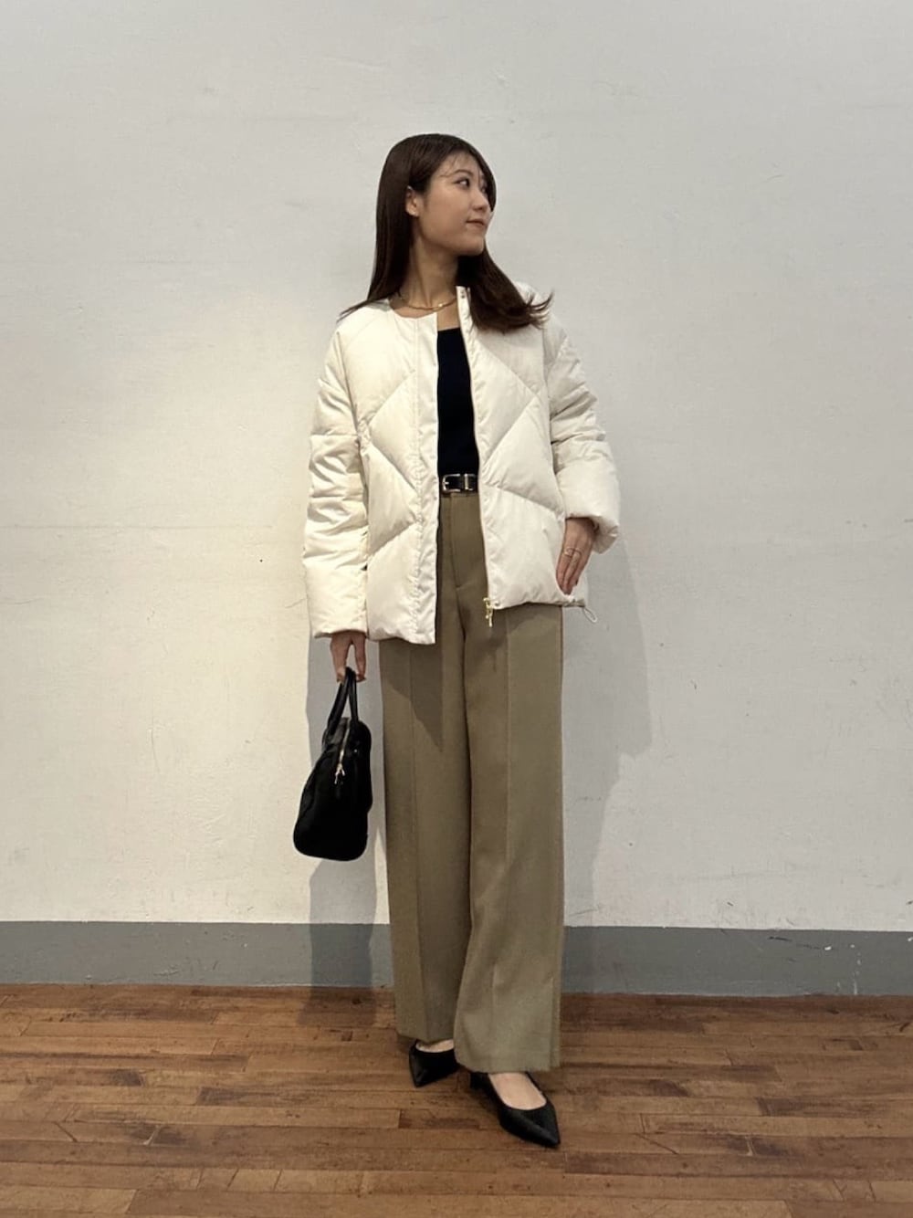 ホワイト系のダウンジャケット/コート、ブラック系のニット/セーター、ベージュ系のスラックスを着用したレディースの冬コーディネートの1枚目の写真