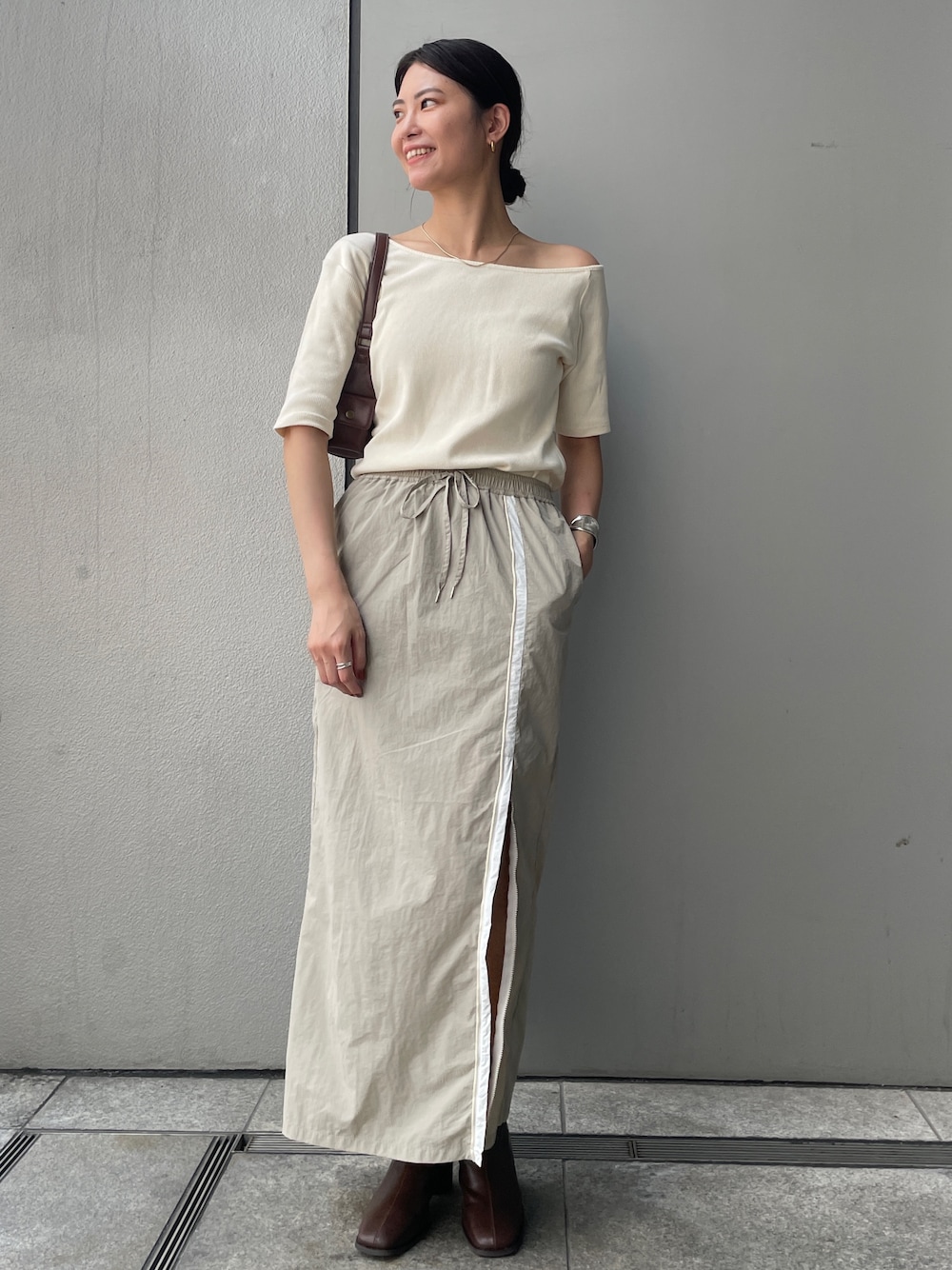 ベージュ系のスカート、ホワイト系のTシャツ/カットソー、ブラウン系のブーツを着用したレディースの夏コーディネートの1枚目の写真
