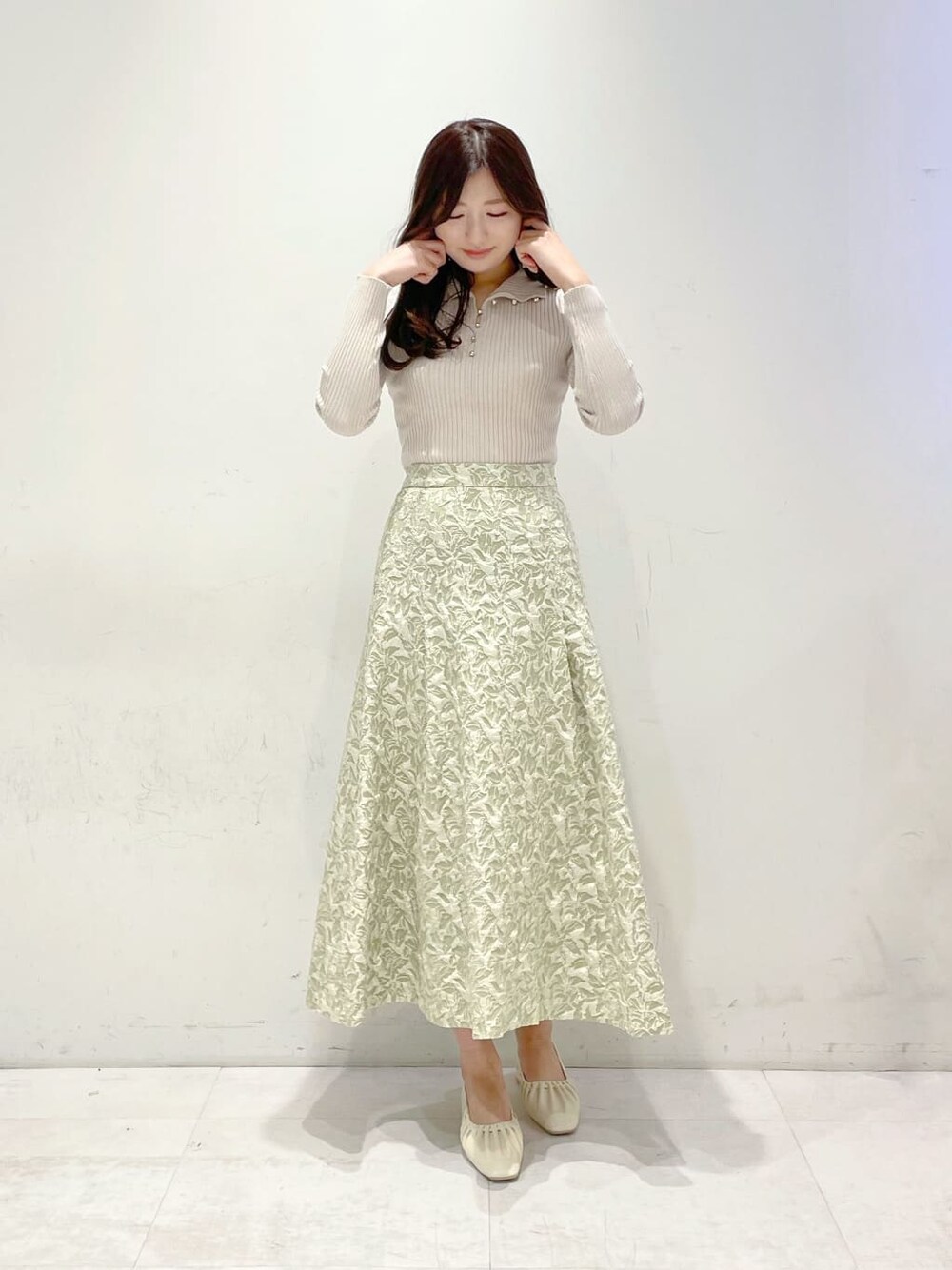 グリーン系のスカート、ホワイト系のパンプス、ベージュ系のニット/セーターを着用したレディースの冬コーディネートの1枚目の写真