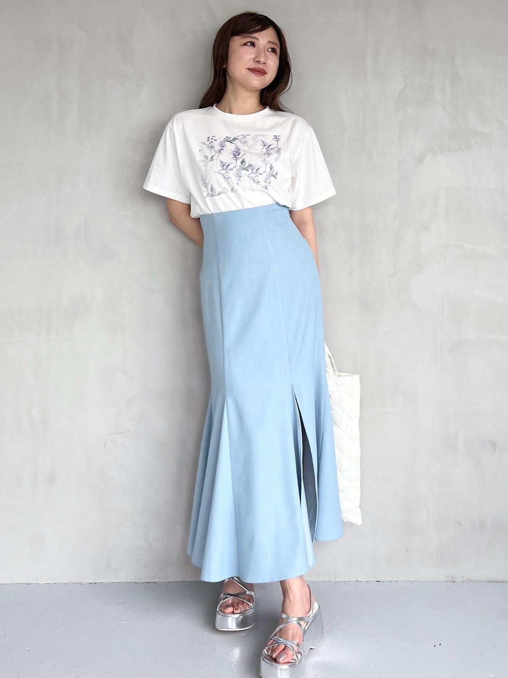 ブルー系のスカート、シルバー系のサンダル、ホワイト系のハンドバッグを着用したレディースの夏コーディネートの1枚目の写真