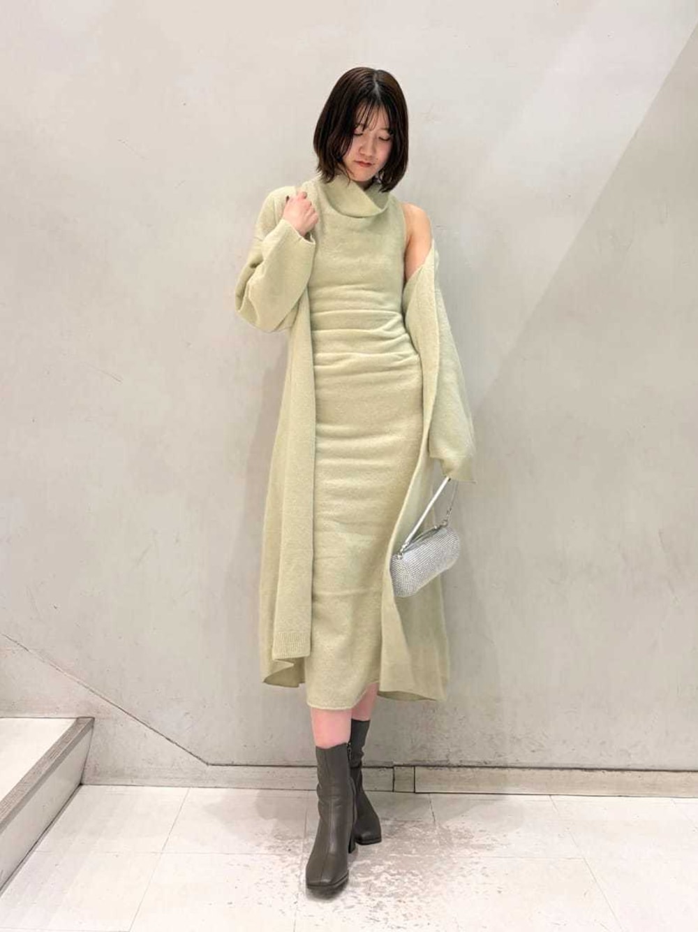 ベージュ系のキャミソール、グリーン系のチェスターコート、グリーン系のワンピースを着用したレディースの冬コーディネートの1枚目の写真
