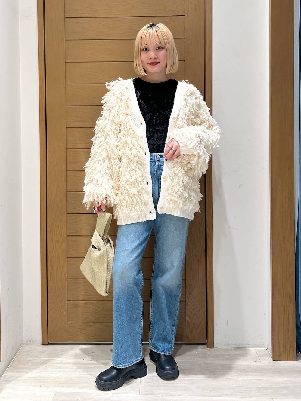 ブルー系のデニムパンツ、ホワイト系のカーディガン/ボレロ、イエロー系のハンドバッグを着用したレディースの冬コーディネートの1枚目の写真