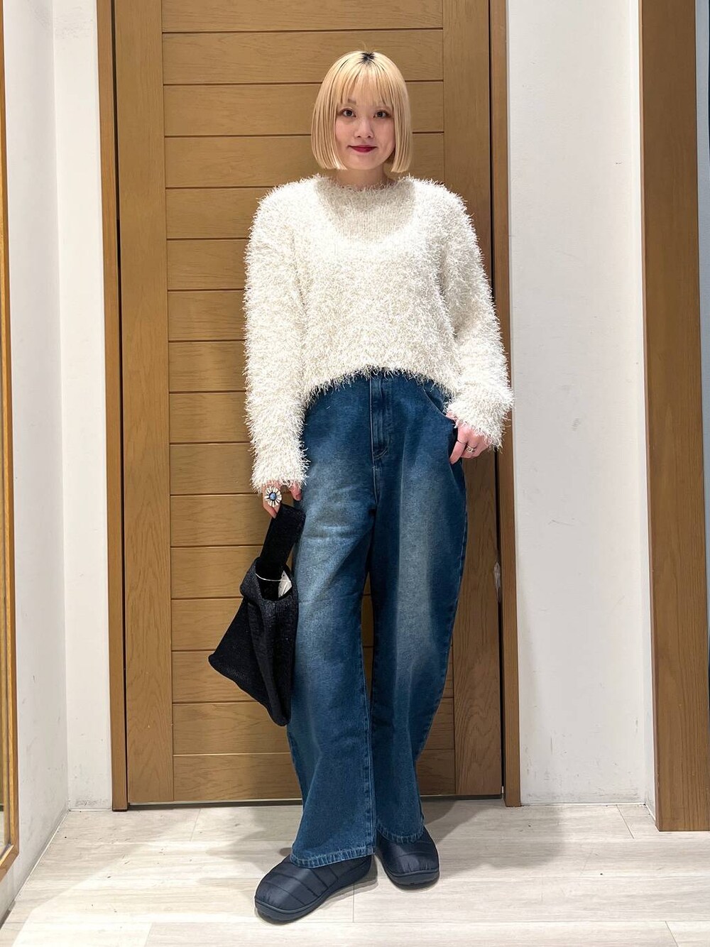 ホワイト系のニット/セーター、ブルー系のデニムパンツ、ブラック系のハンドバッグを着用したレディースの冬コーディネートの1枚目の写真