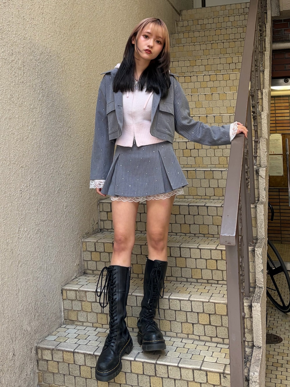 グレー系のテーラードジャケット、グレー系のスカート、ピンク系のパーカーを着用したレディースの冬コーディネートの1枚目の写真