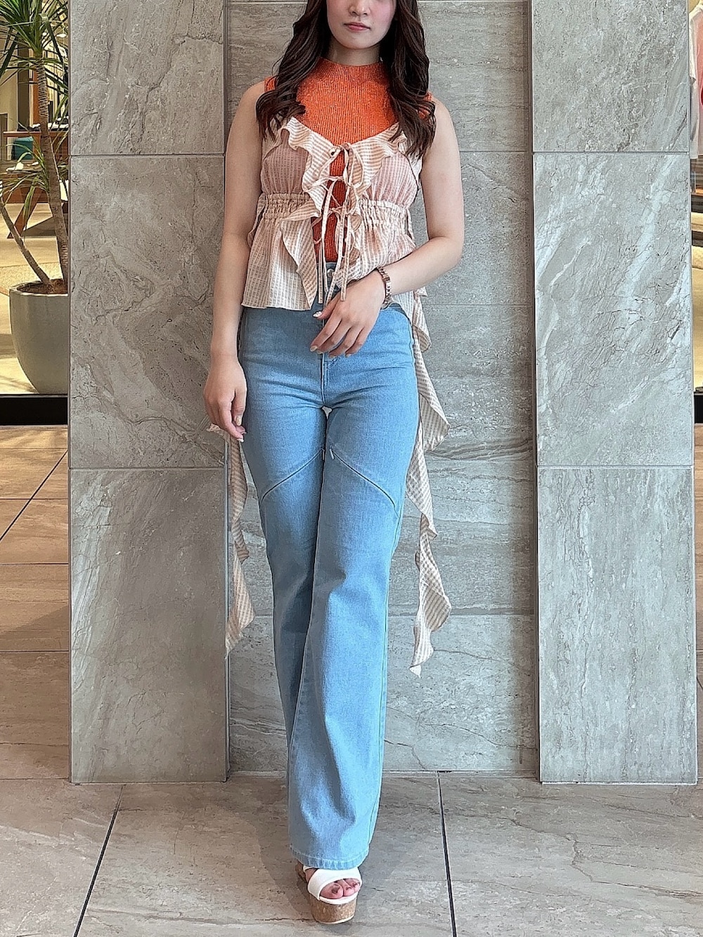 ブルー系のデニムパンツ、オレンジ系のニット/セーター、オレンジ系のキャミソールを着用したレディースの夏コーディネートの1枚目の写真