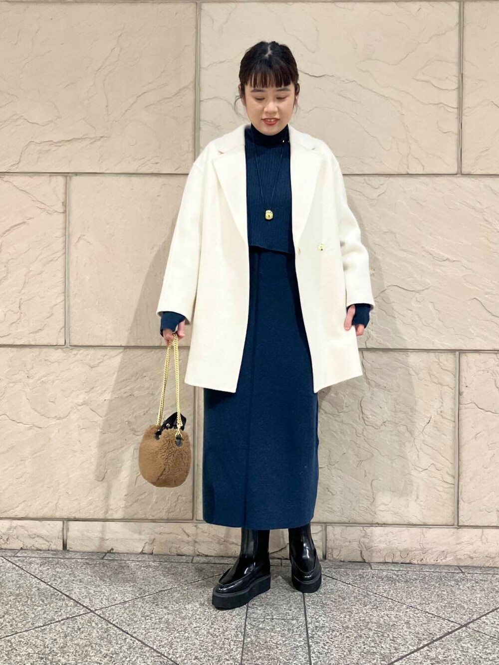 ホワイト系のチェスターコート、ブルー系のワンピース、ブラウン系のショルダーバッグを着用したレディースの冬コーディネートの1枚目の写真