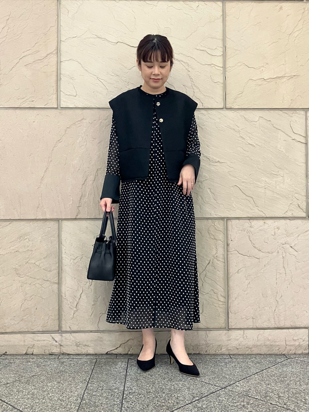 ブラック系のベスト、ブラック系のワンピース、ブラック系のパンプスを着用したレディースの秋コーディネートの1枚目の写真