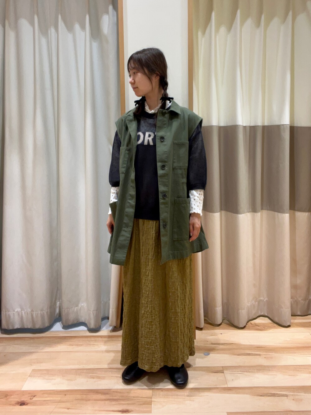 グリーン系のベスト、イエロー系のTシャツ/カットソー、グレー系のニット/セーターを着用したレディースの秋コーディネートの1枚目の写真